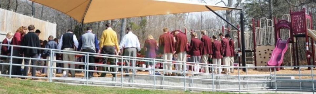Foundational Beliefs Banner Teachers and students praying to dedicate new school playground